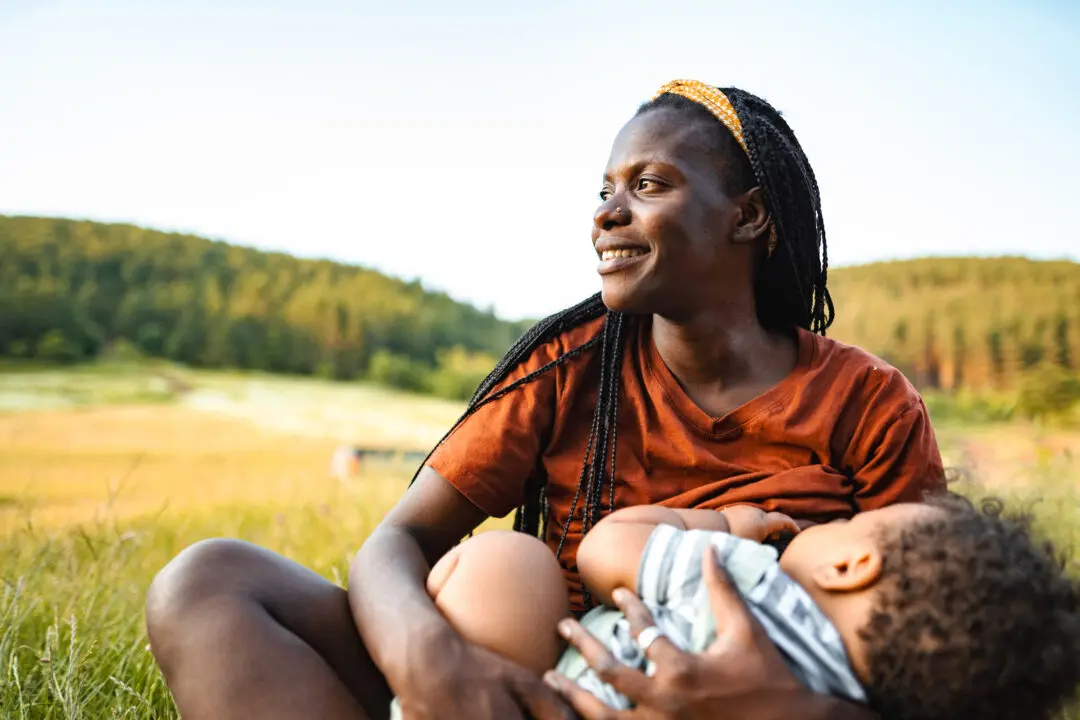 A woman breastfeeding her baby outdoors in a natural setting.