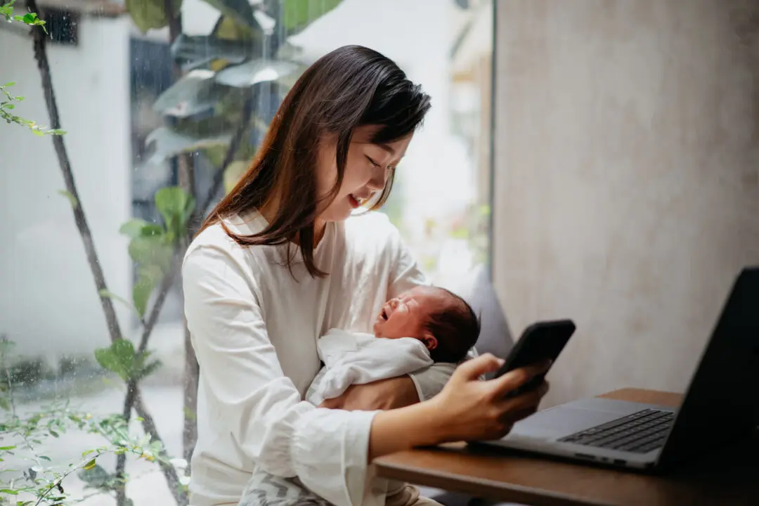 A woman holding a newborn while looking at her phone.